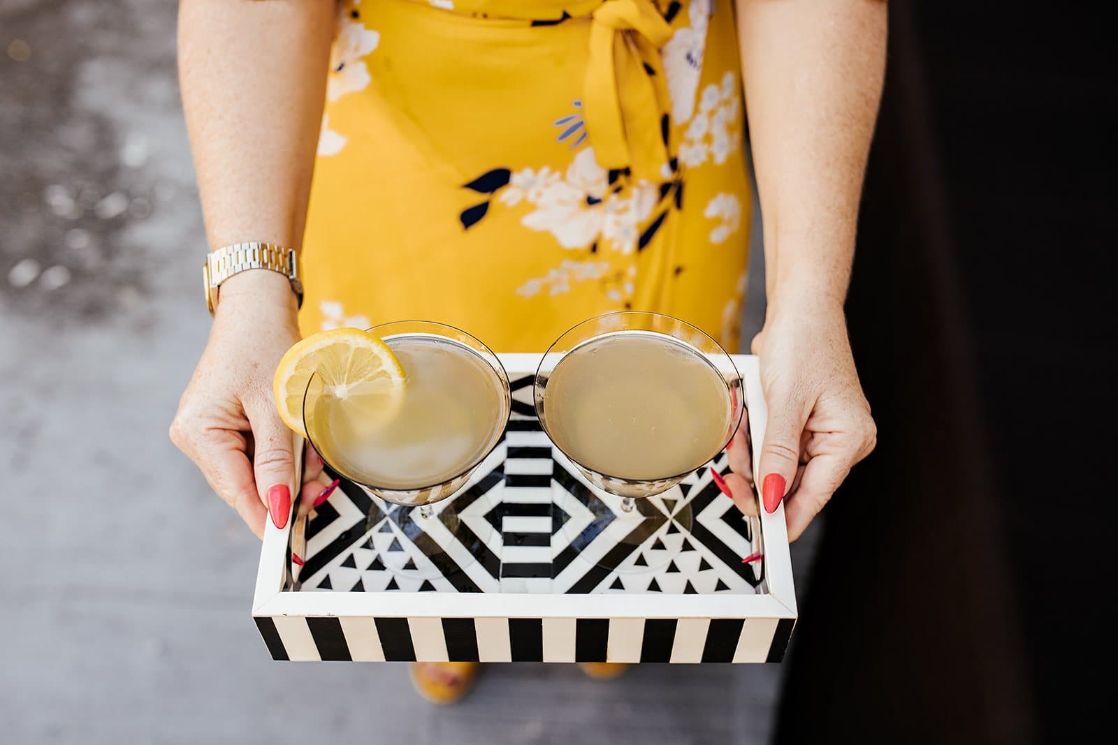 Host holding a black-and-white tray of cocktails