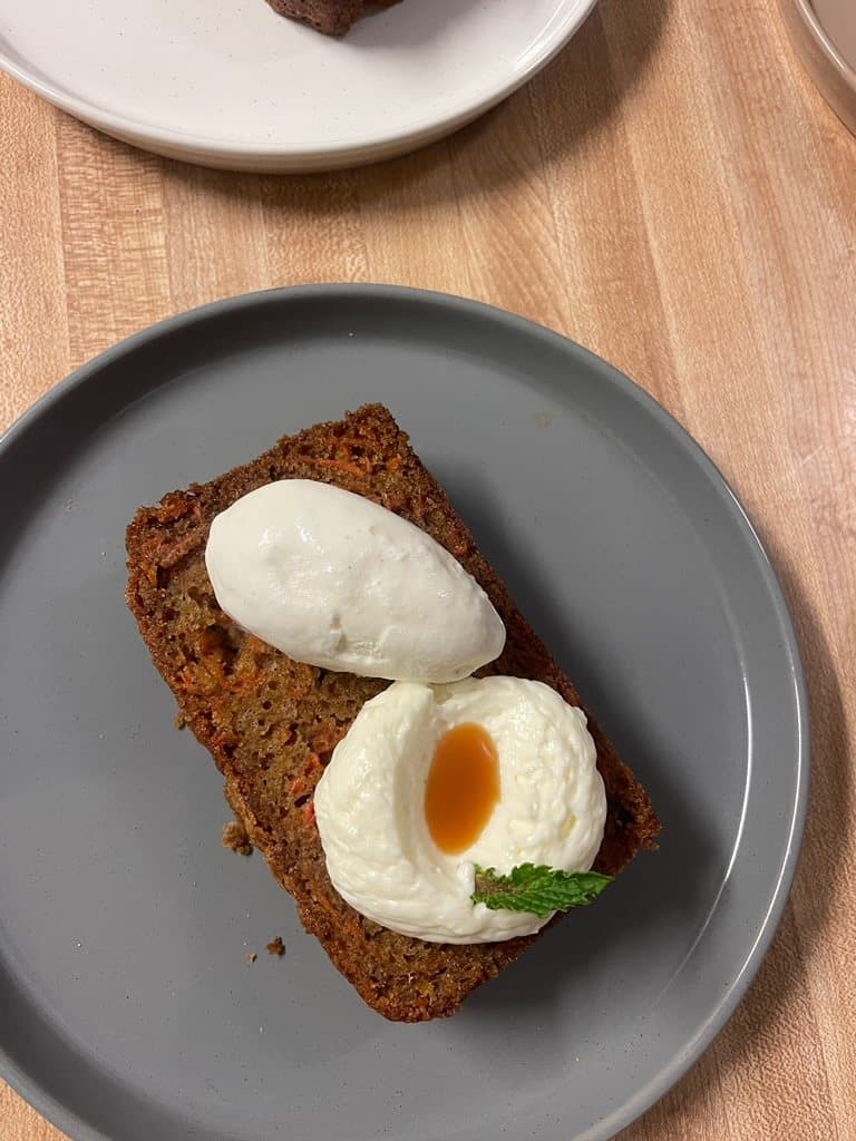 Slice of cake topped with two quenelles of cream on a grey plate