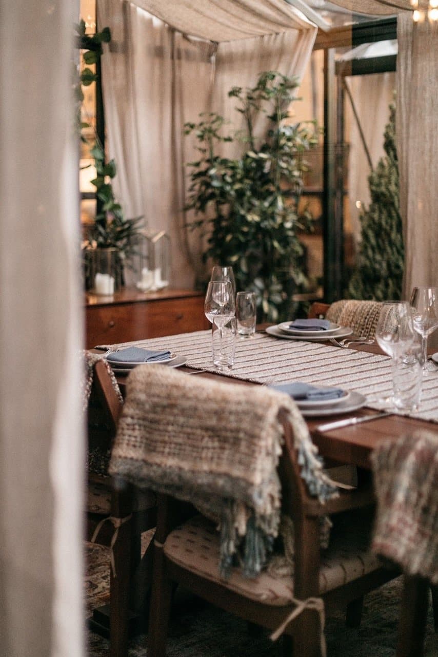 Dining room with a set wooden table, woven throws and draped curtains