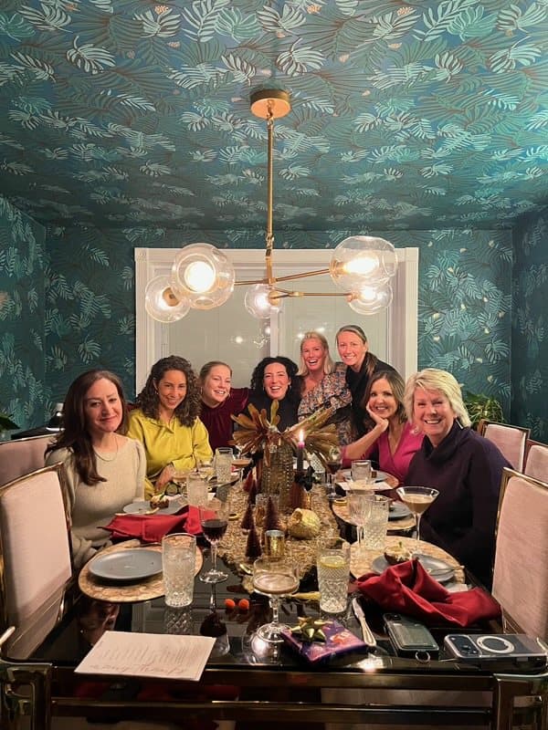 Guests smiling around a candlelit dinner table under a statement chandelier
