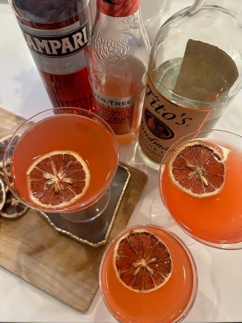 Grapefruit cocktails with dried citrus wheels beside Campari and Tito's bottles