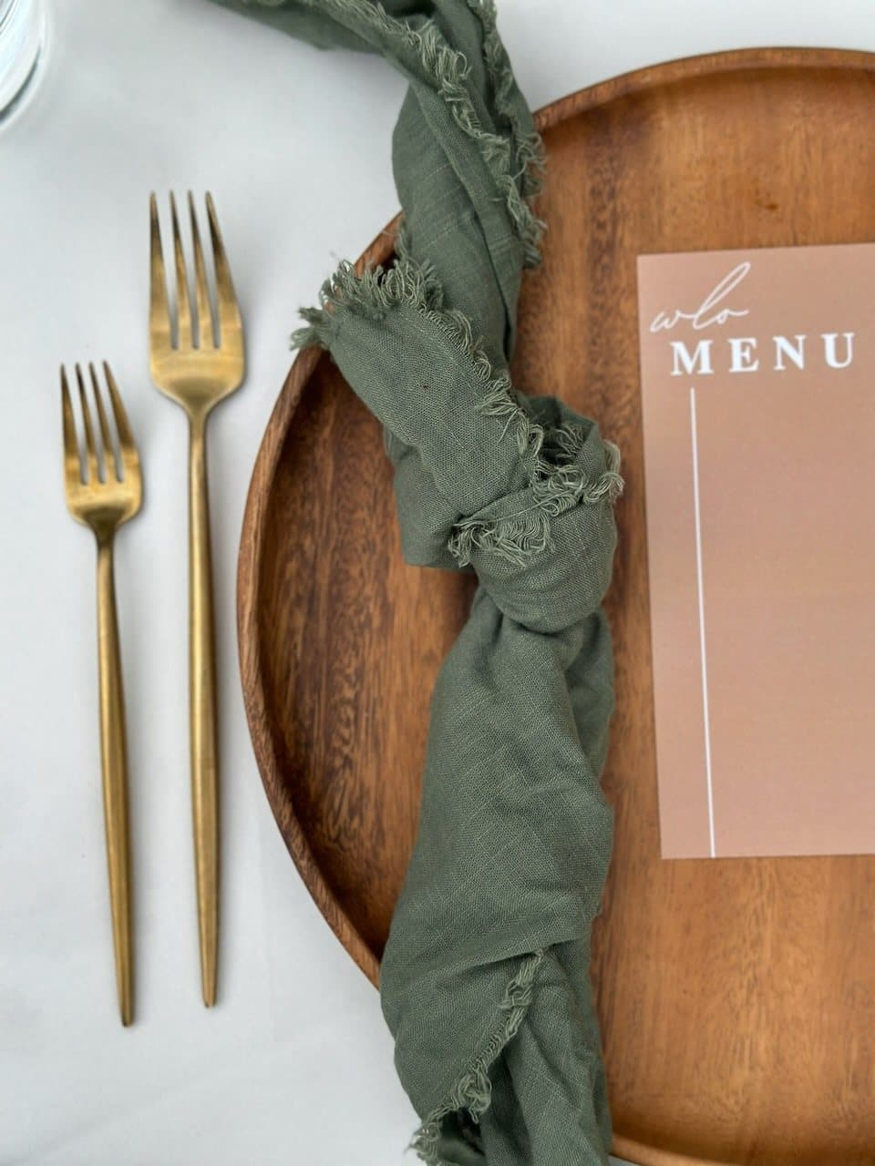 Menu card with gold forks and a green linen napkin on a wooden charger