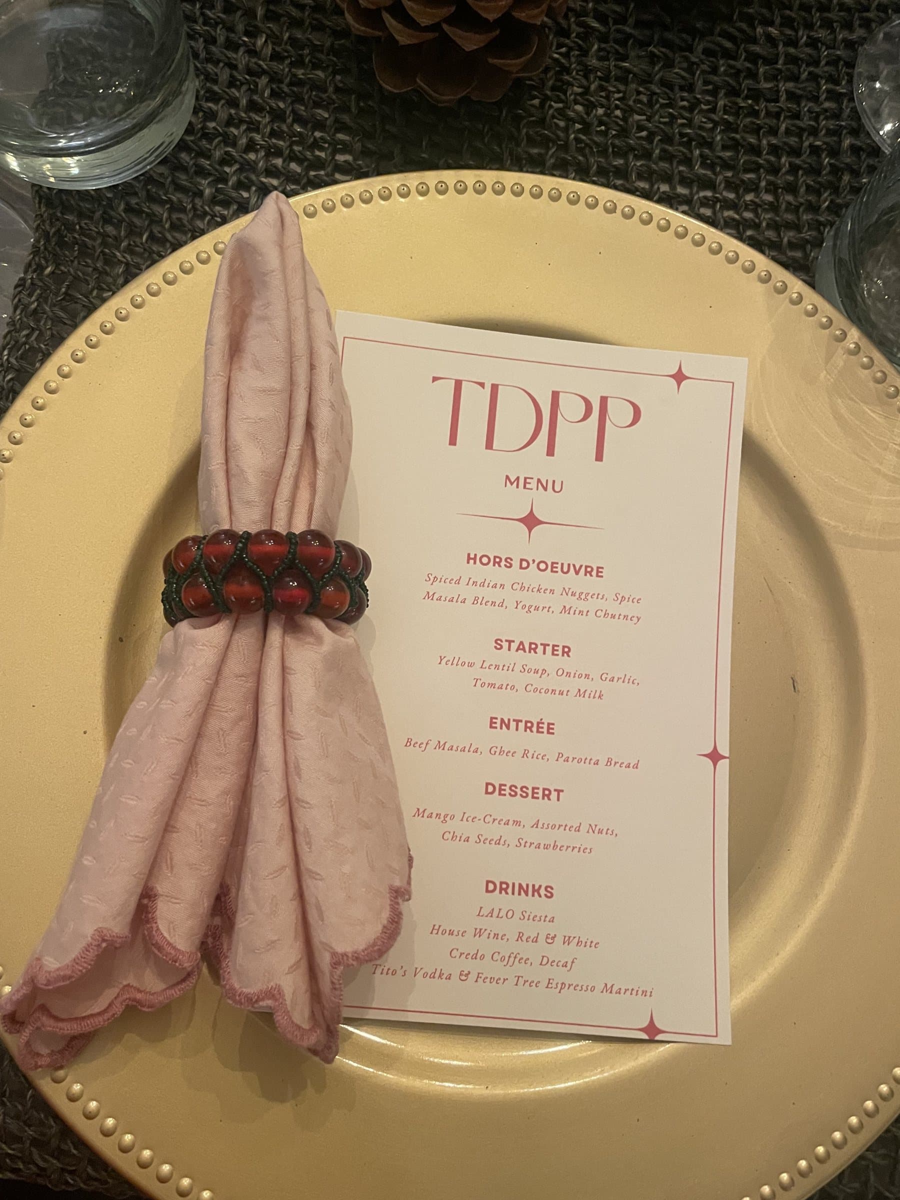 Gold charger place setting with a pink napkin and a TDPP dinner menu