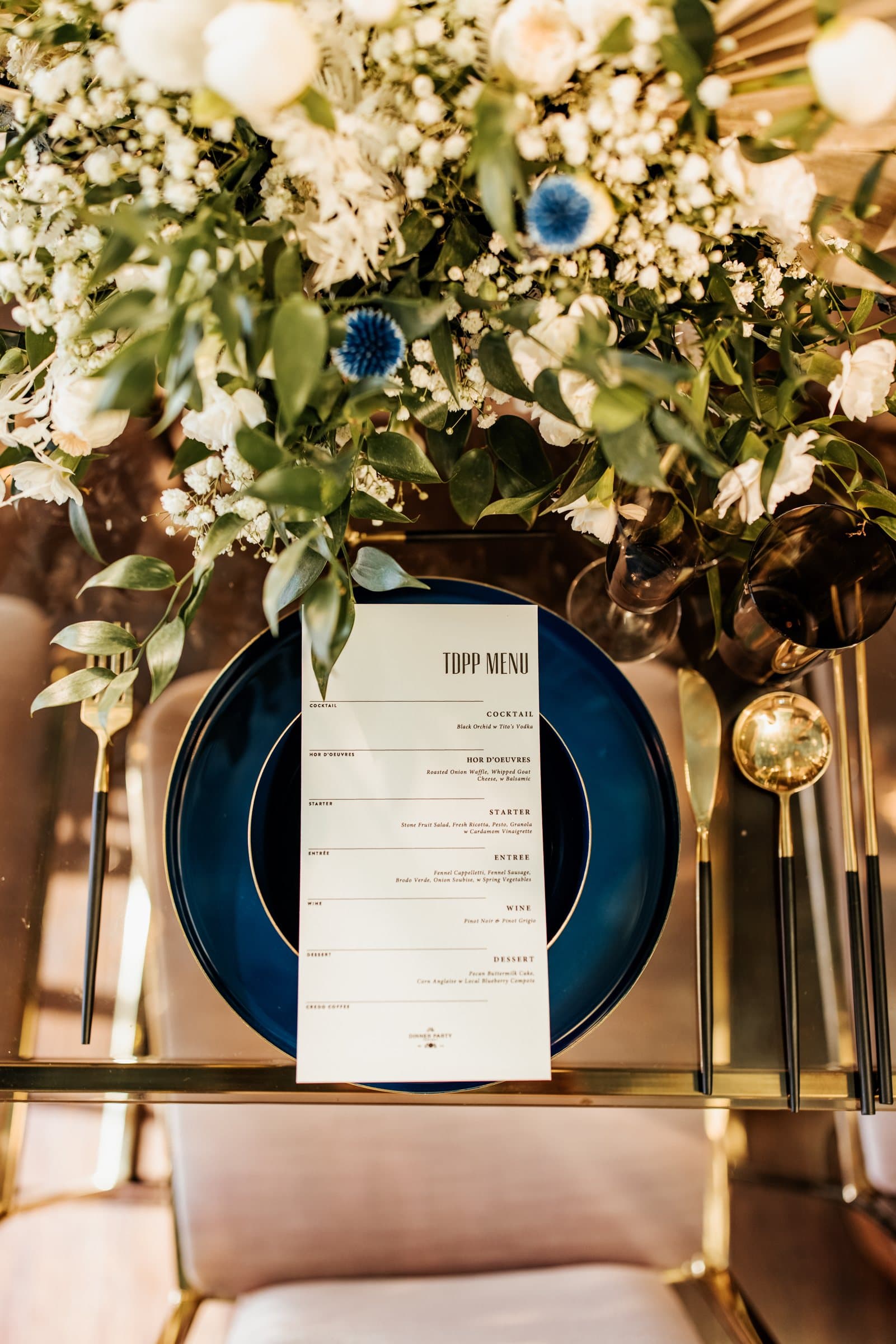 Dinner table set with a TDPP menu on a blue charger beneath a garland of white flowers