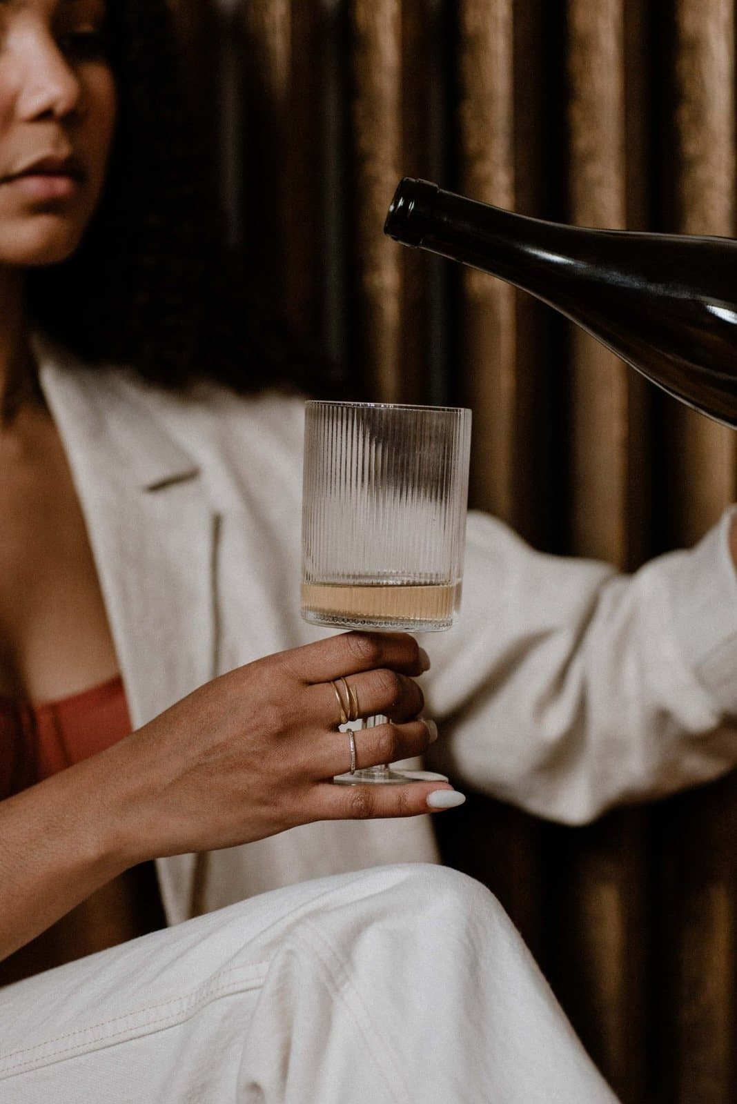 Wine being poured into a ribbed glass held by a guest in a white blazer